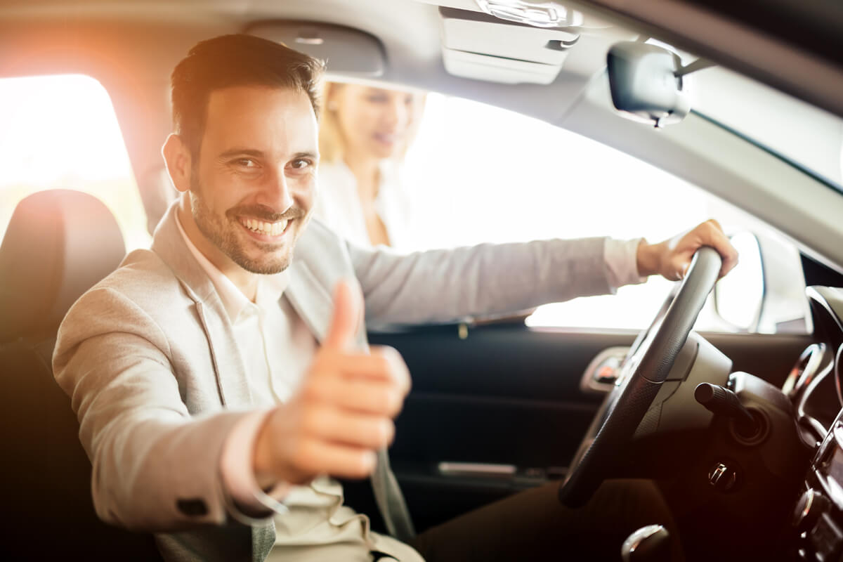 Person sitzt im Auto und zeigt einen Daumen nach oben
